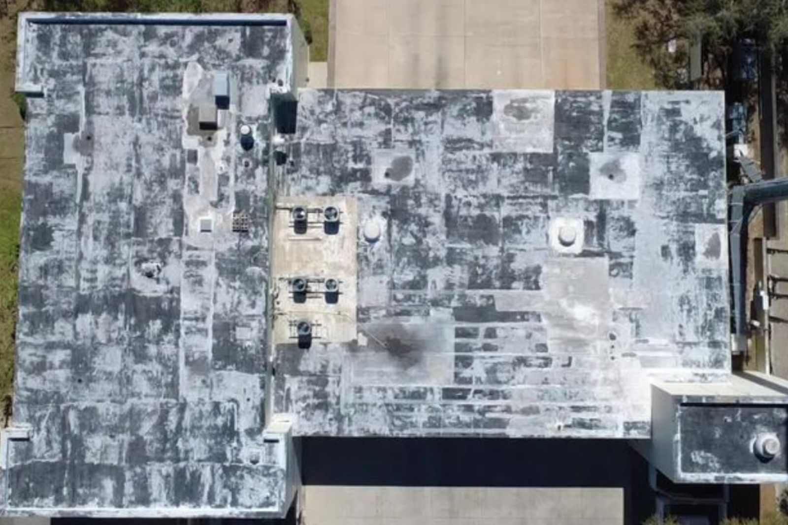 Aerial view of a worn commercial flat roof with patchwork areas before repair or coating.