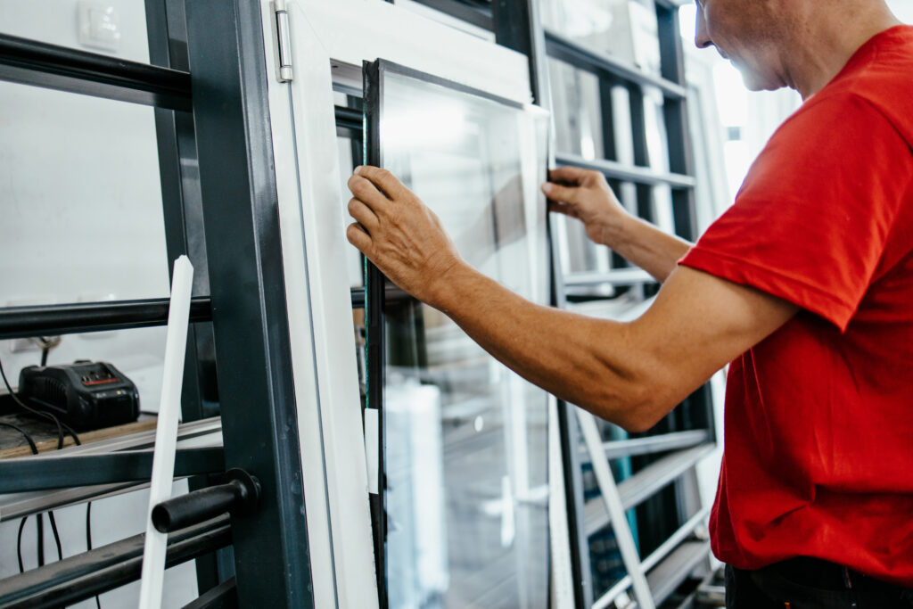 Worker in a red shirt fits a glass window pane into a frame in a workshop or showroom.