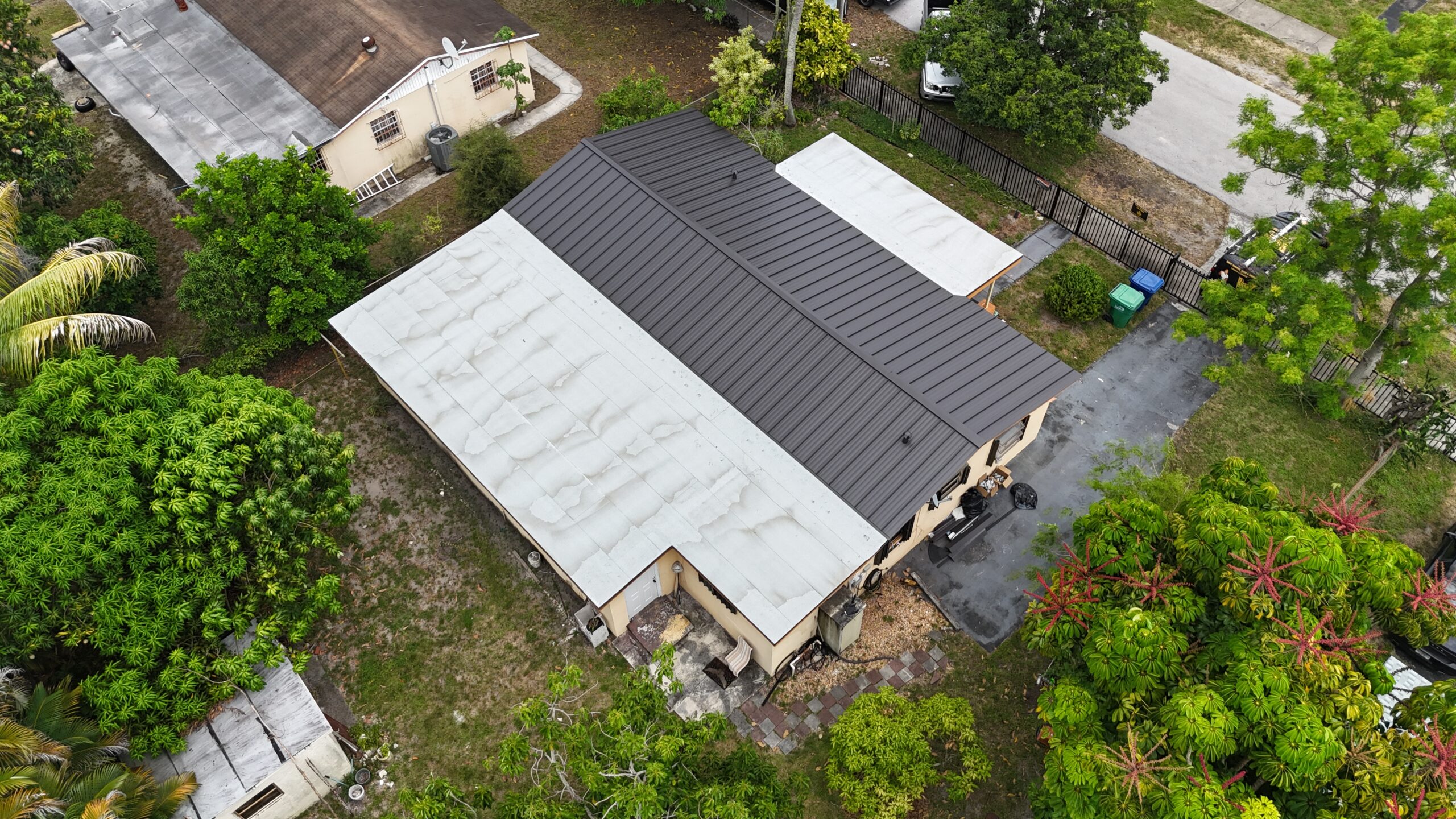 Close-up of the installed metal ridge and standing seams beside white flat-roof sections in Miami Gardens