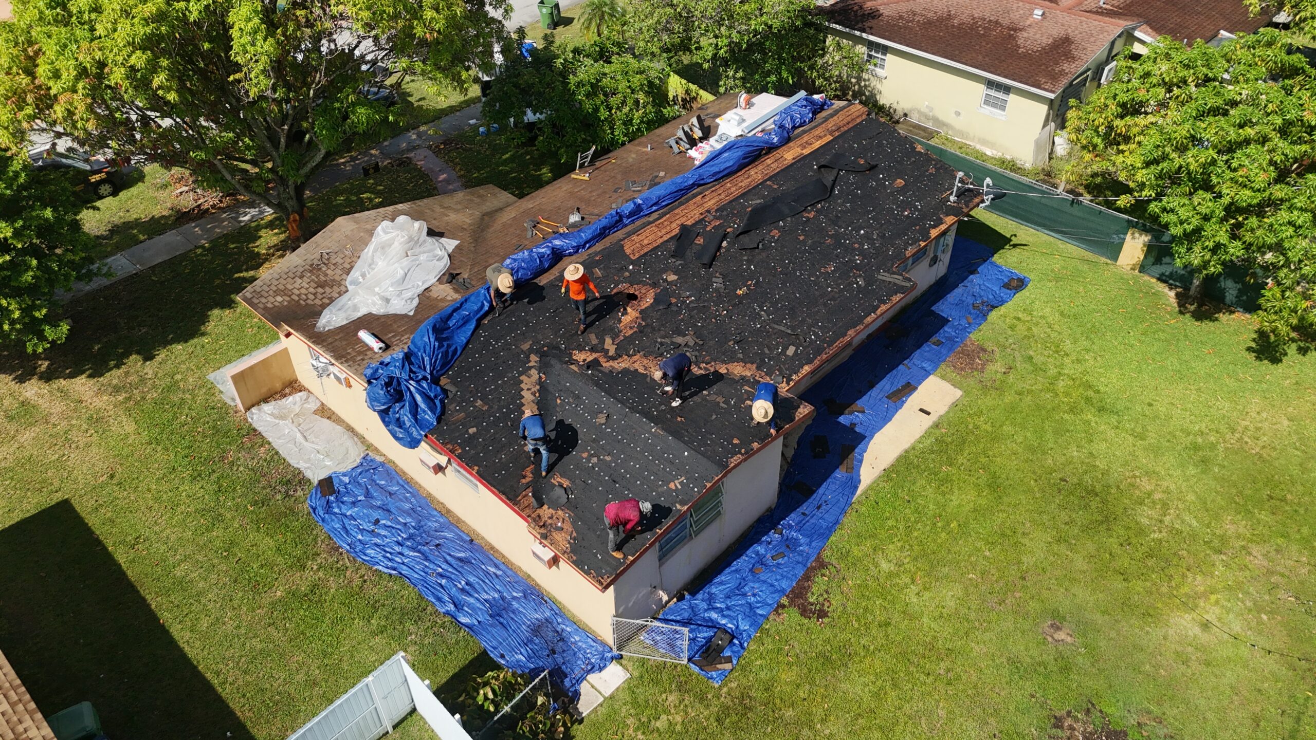 Roofing crew removing layers with blue tarps around the Cutler Bay home